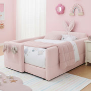 Pink children's bed with decorative elements in a room with pink walls and toys on the floor.